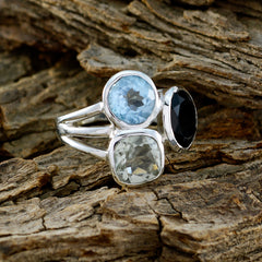 Meera multicolor gemstone trilogy ring with blue, black, and clear stones set in silver band on wood