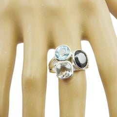 Meera multicolor gemstone trilogy ring with blue, black, and clear stones on a display hand