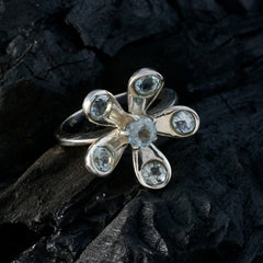 Claire blue floral gemstone ring with silver petals and clear blue stones on dark textured surface