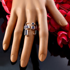 blue gemstone signet ring with three rectangular and one round blue stone on gold band shown on mannequin hand with red flowers