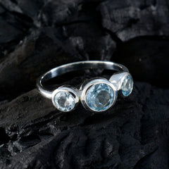 Natcha silver band blue gemstone trilogy ring with three bezel set round blue stones on dark textured rock