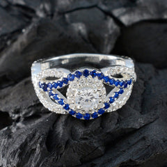 Isabella silver blue halo ring with central clear stone and blue sapphires on black textured background