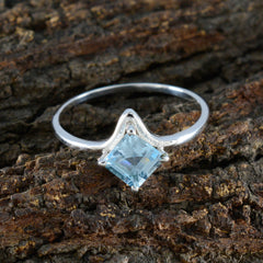 Yan silver ring with a princess cut blue solitaire gemstone ring set in a delicate prong setting on bark