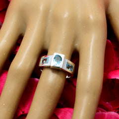 Ellie silver ring with three blue gemstones on display hand against pink petals blue trilogy ring for women