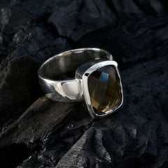 Lily brown solitaire ring with cushion cut faceted brown gemstone in polished silver bezel setting on dark textured rock background