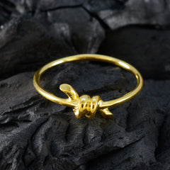 Milagros delicate gold twist ring for women with knotted detail on a thin band on dark stone background