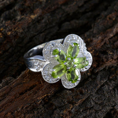 Victoria green gemstone statement ring with flower-shaped design and silver band on textured wood