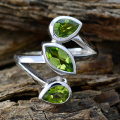 Mariana silver green gemstone trilogy ring with three pear and marquise peridot stones on textured wood