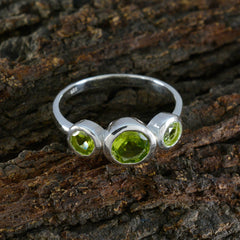 Lily silver green gemstone trilogy ring with three bezel set peridot stones on slender band on rustic wood background
