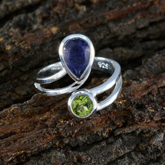 Ida toi et moi gemstone ring sterling silver with pear shaped blue gemstone and round peridot on bark background