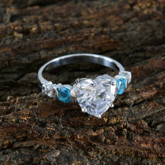 Nova white gemstone heart ring with silver band and blue side stones on rustic wood background