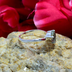 Violet light green solitaire ring with silver band displayed on textured stone with red flower background