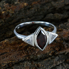 Emi luxurious red gemstone ring with silver band and clear side stones on rustic background