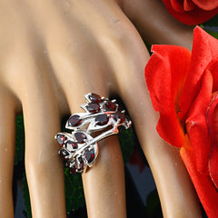 Dewi modern red gemstone ring with intricate leaf design on finger next to red rose petals