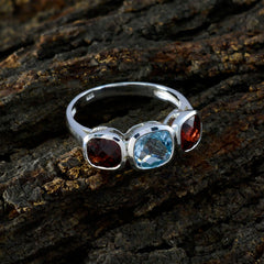Ida multicolor trilogy gemstone ring with red and blue stones set in silver band on textured surface