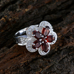 Isla red floral gemstone ring with silver band and red petals on textured wood background