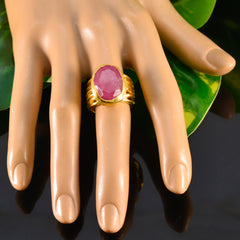 Lara red solitaire ring featuring an oval faceted red gemstone in a polished gold band on a display hand