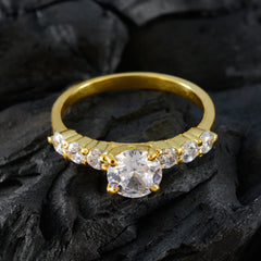 Dewi white gemstone gold ring with a large center stone and smaller surrounding stones on a textured black surface