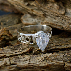 Skylar white solitaire ring with pear-shaped gemstone and intricate silver band design on rustic wood