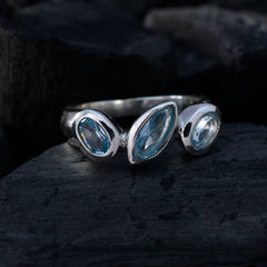 Laura artisan blue gemstone ring with three blue stones set in a silver band on a dark textured surface