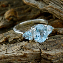 Chloe blue gemstone trilogy ring with three light blue stones set in silver band on rustic wood