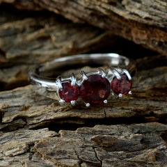 Hua red gemstone trilogy ring with three round red stones set in silver band on rustic wood