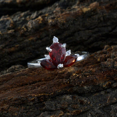 Liyana silver red gemstone trilogy ring with pear-shaped red stones and small clear accents on rustic wood