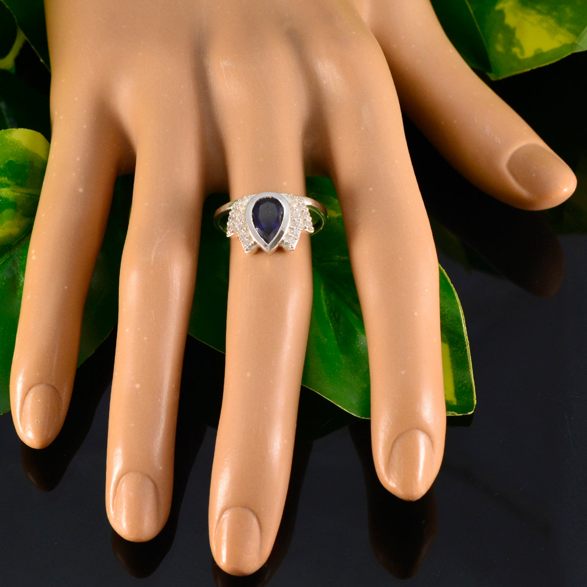 Dewi blue gemstone halo ring with pear-shaped center stone and diamond accents on display hand