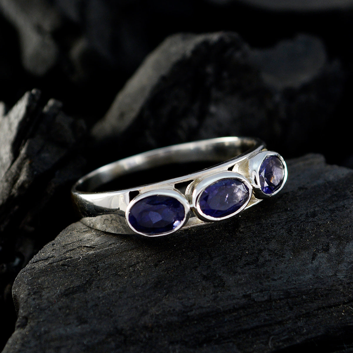 Lily blue trilogy gemstone ring with three oval blue stones set in silver band on dark background