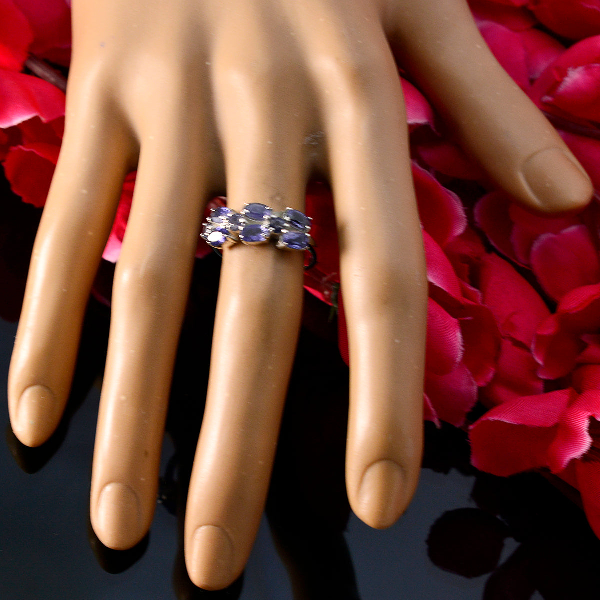 blue gemstone hexa ring on mannequin hand with three blue stones and silver band over pink petals