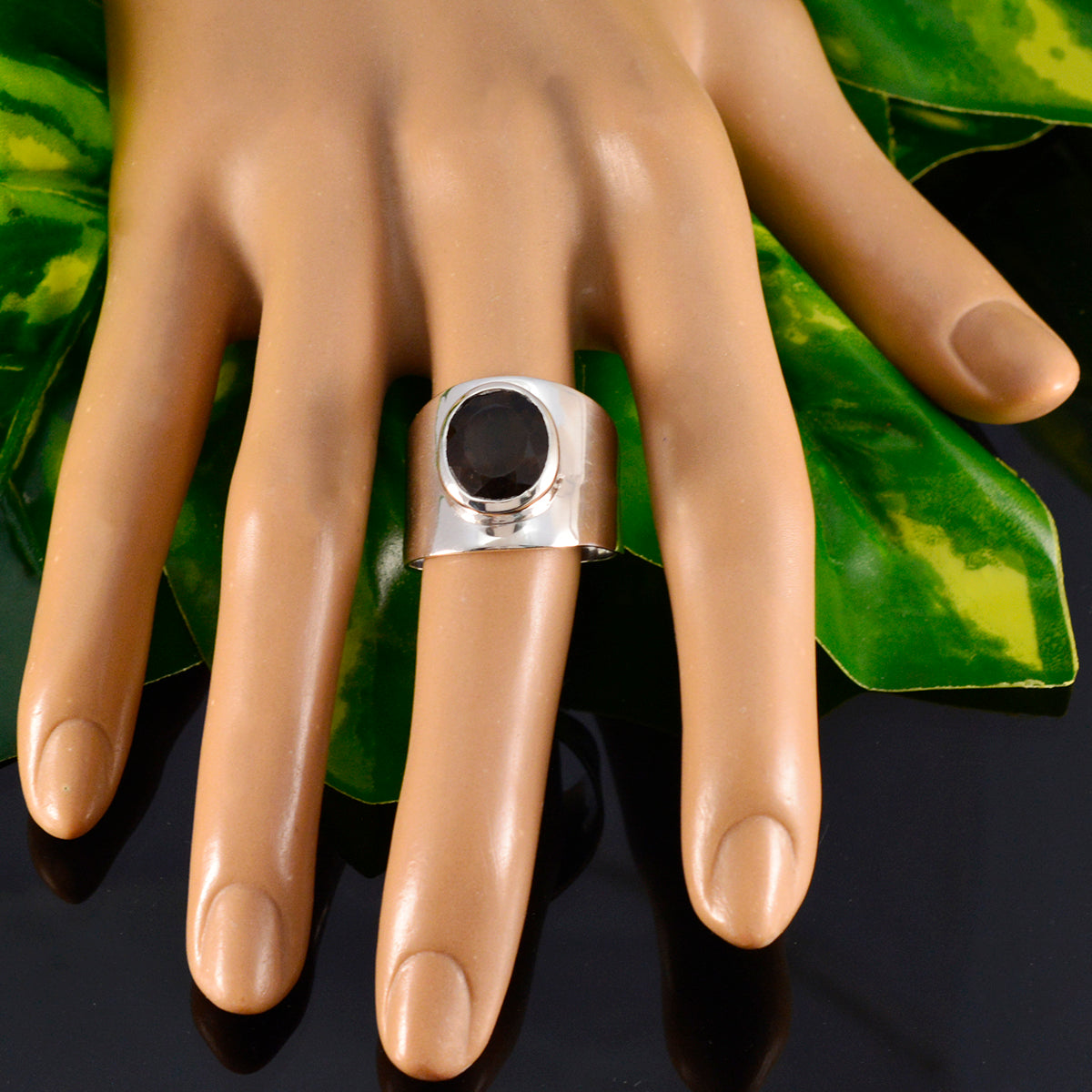 Florencia silver ring with large dark gemstone displayed on mannequin hand against green leaves