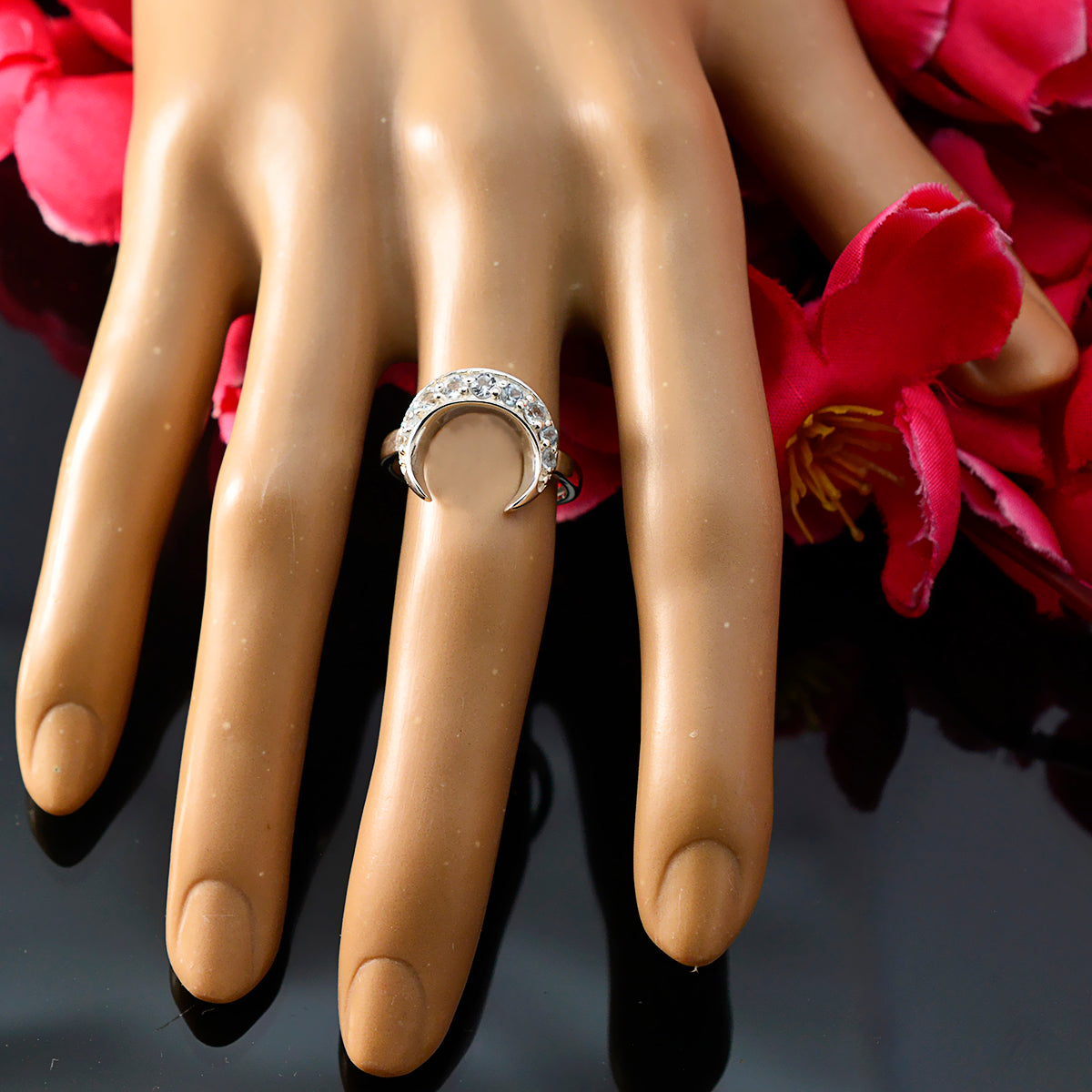 Naomi artisan blue gemstone ring with crescent moon design worn on a display hand with red flowers background