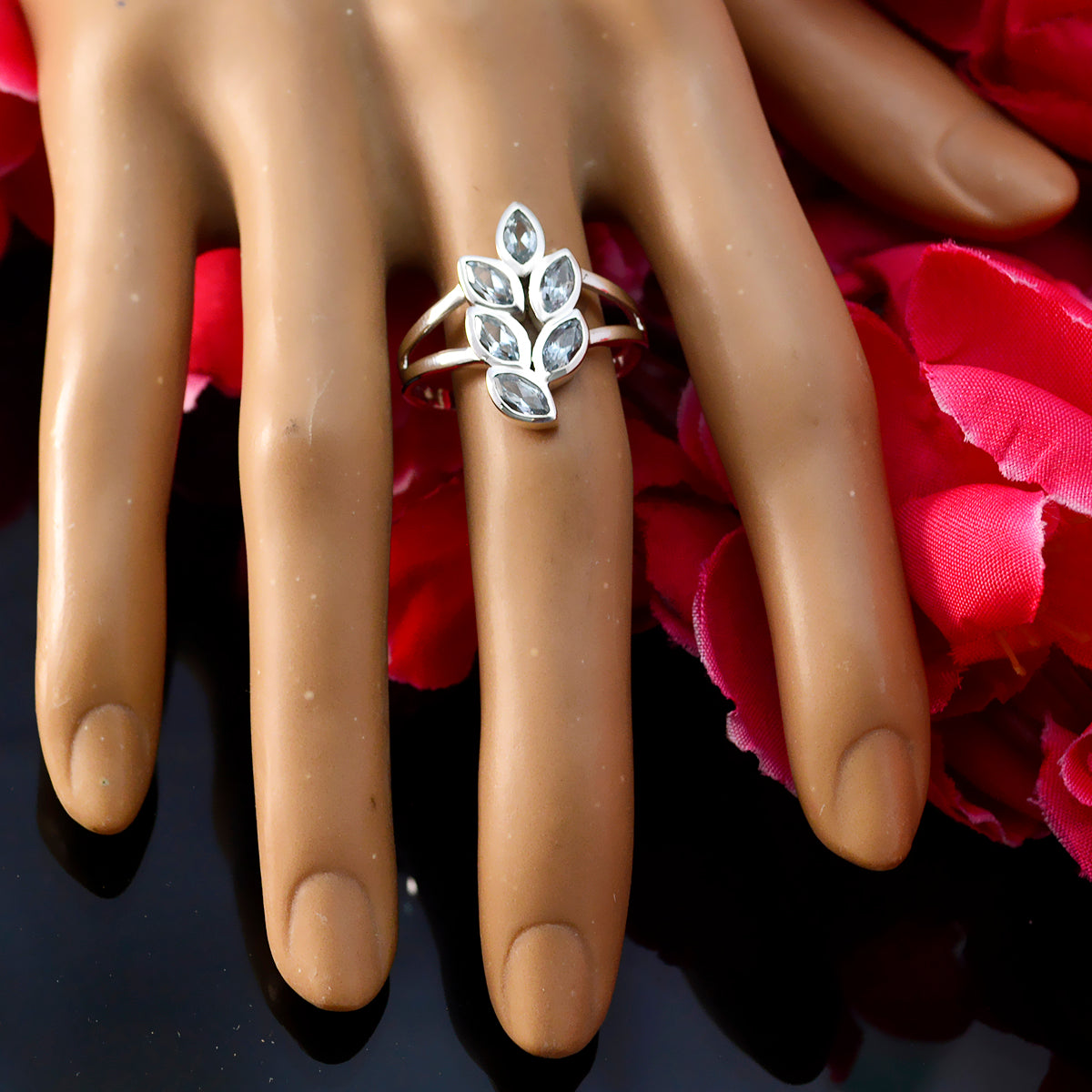 Rebeca artisan blue gemstone ring with silver leaf design on display hand with red petals background