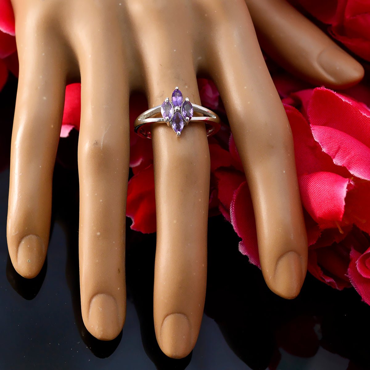 Layla artisan purple gemstone ring with three marquise amethyst stones on silver band displayed on mannequin hand with rose petals