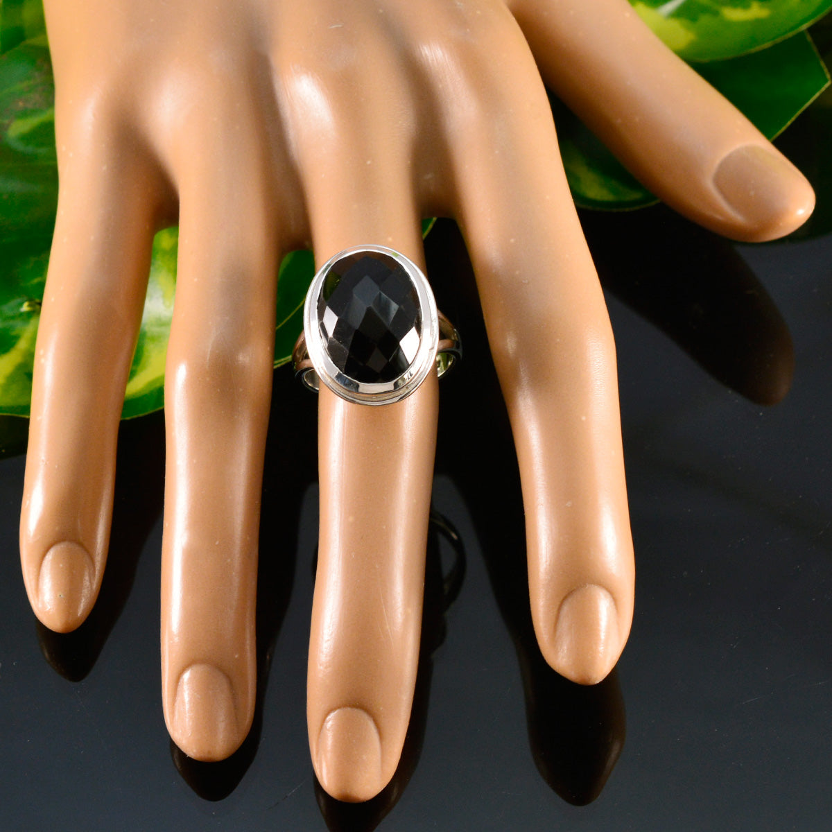 Dewi black solitaire ring for women with faceted oval black stone in silver bezel setting on mannequin hand