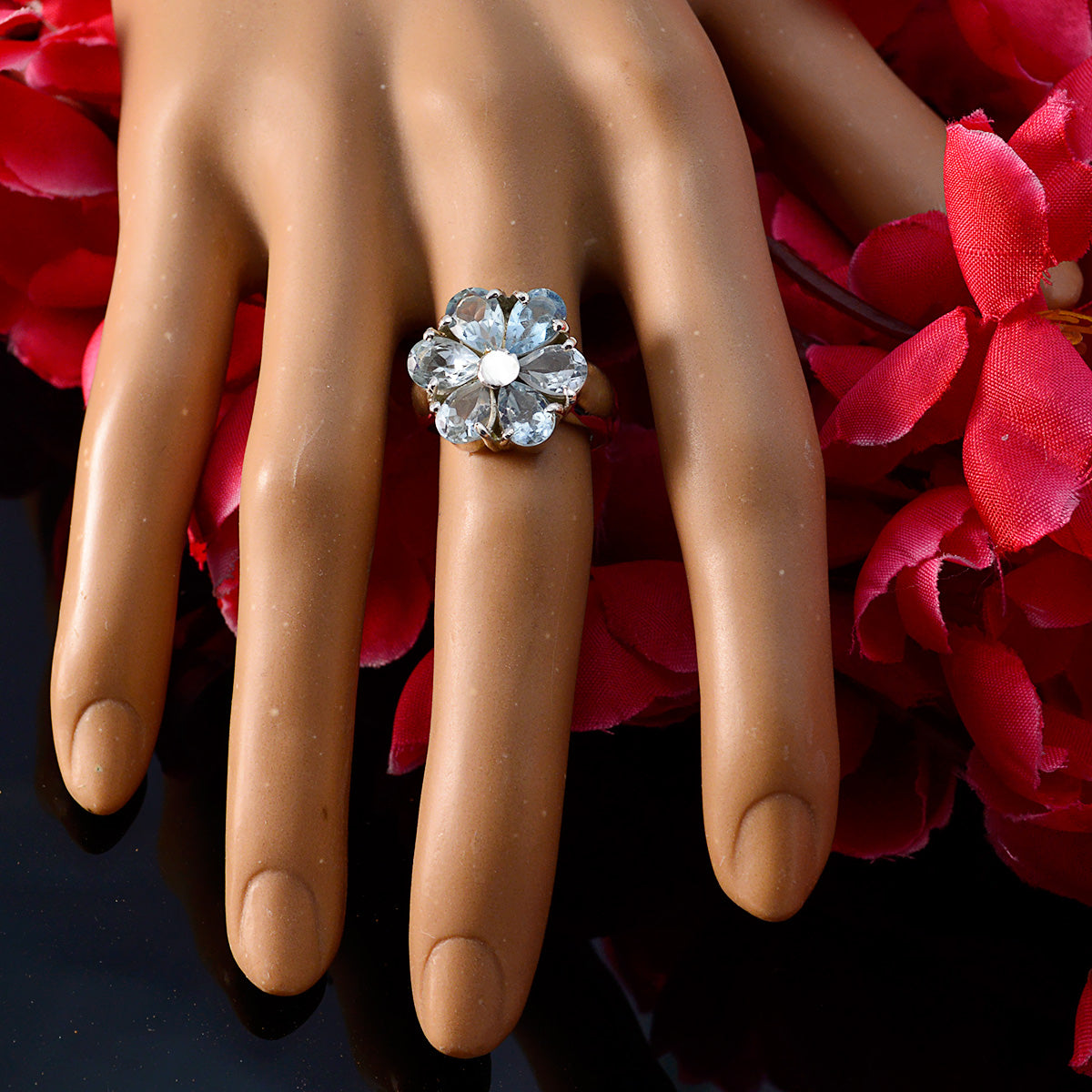 Lucia blue floral gemstone ring on mannequin hand with red flowers background