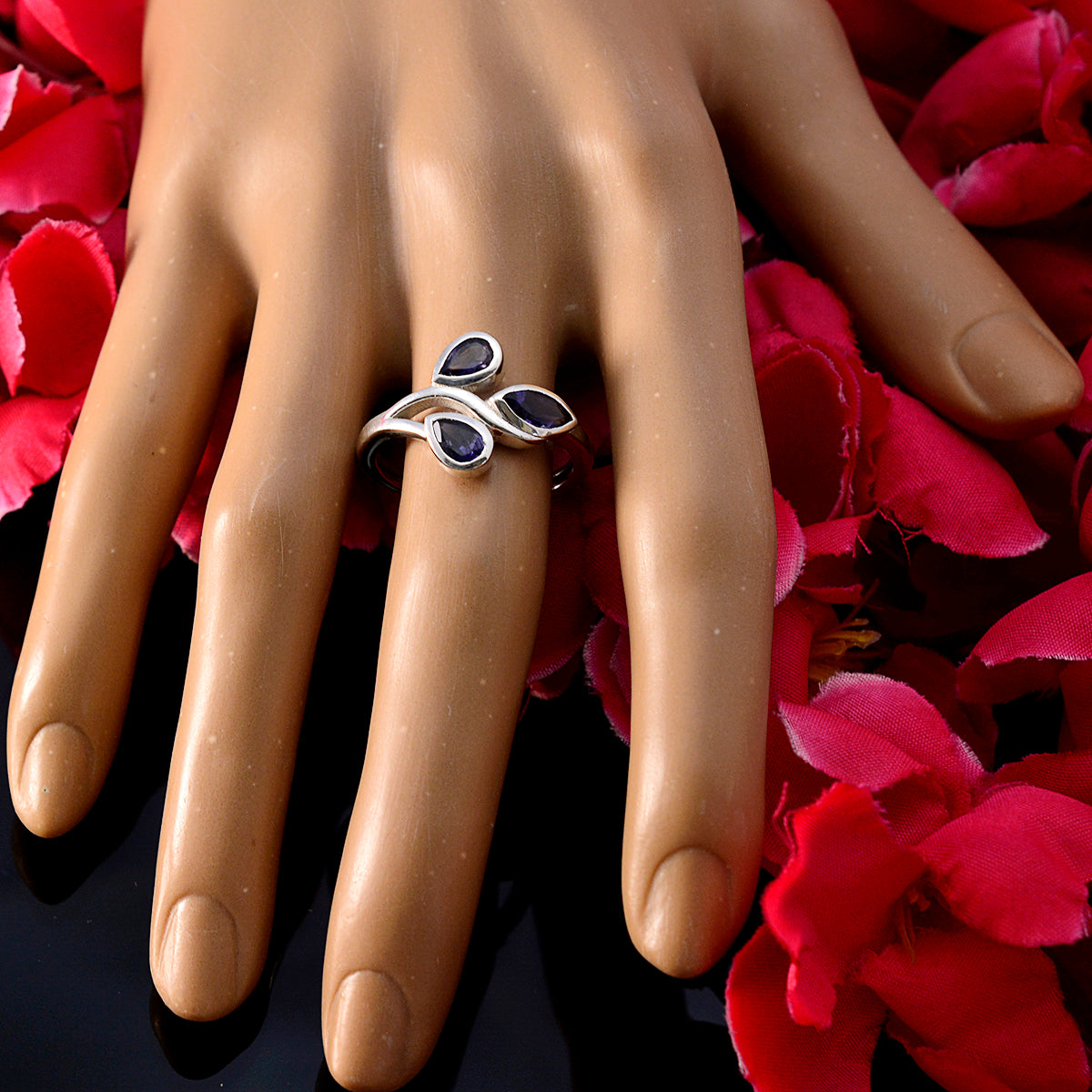 Micaela blue gemstone trilogy ring with three blue stones on silver band displayed on hand with red petals