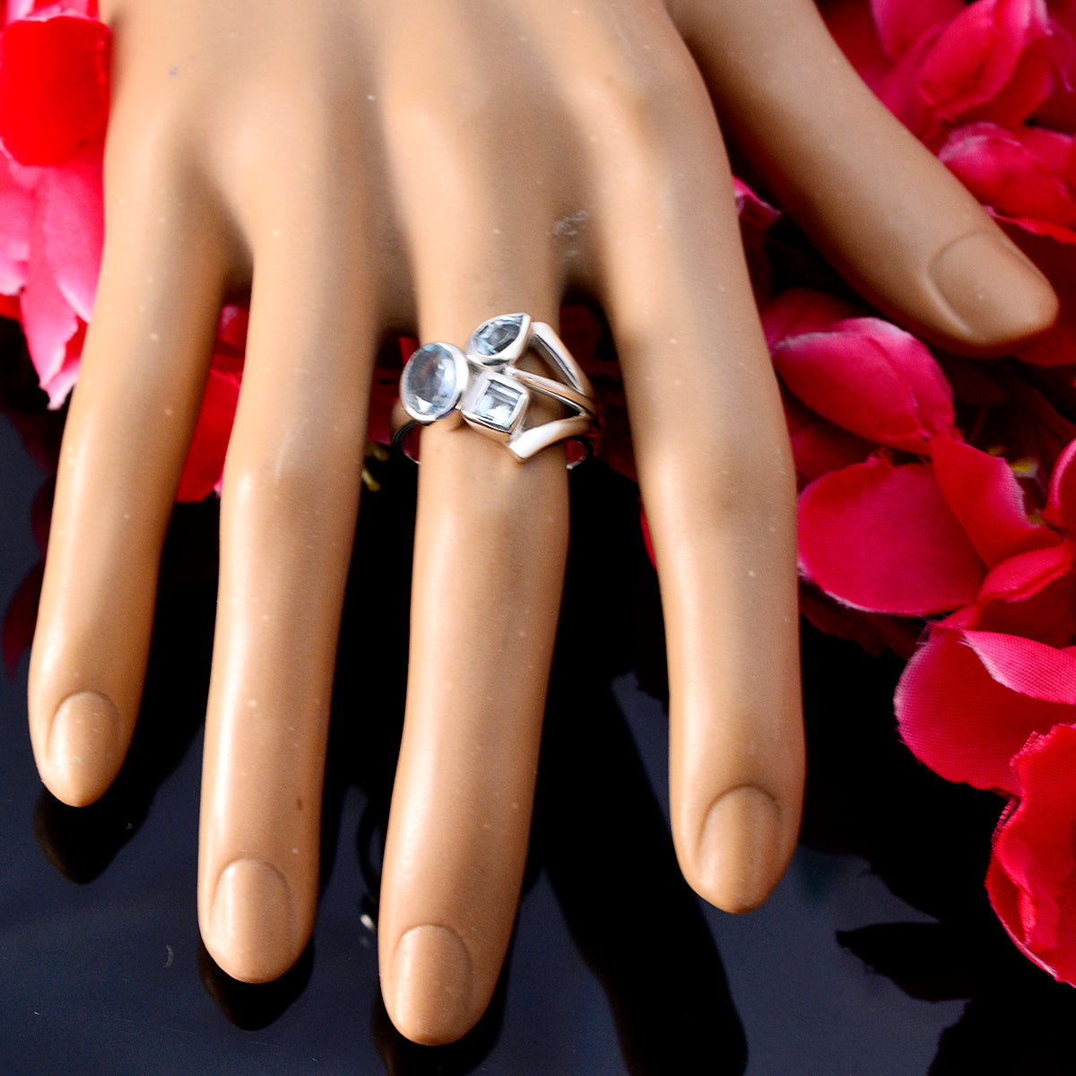 Julieta silver blue gemstone trilogy ring with round pear and square stones on a display hand over pink petals