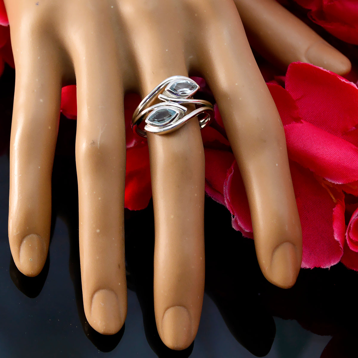 Micaela silver blue toi et moi ring with two blue stones displayed on a hand model with red petals