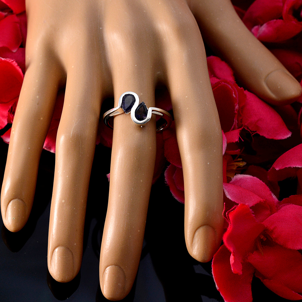 Meera blue toi et moi ring with two blue stones on silver band displayed on hand with red flowers