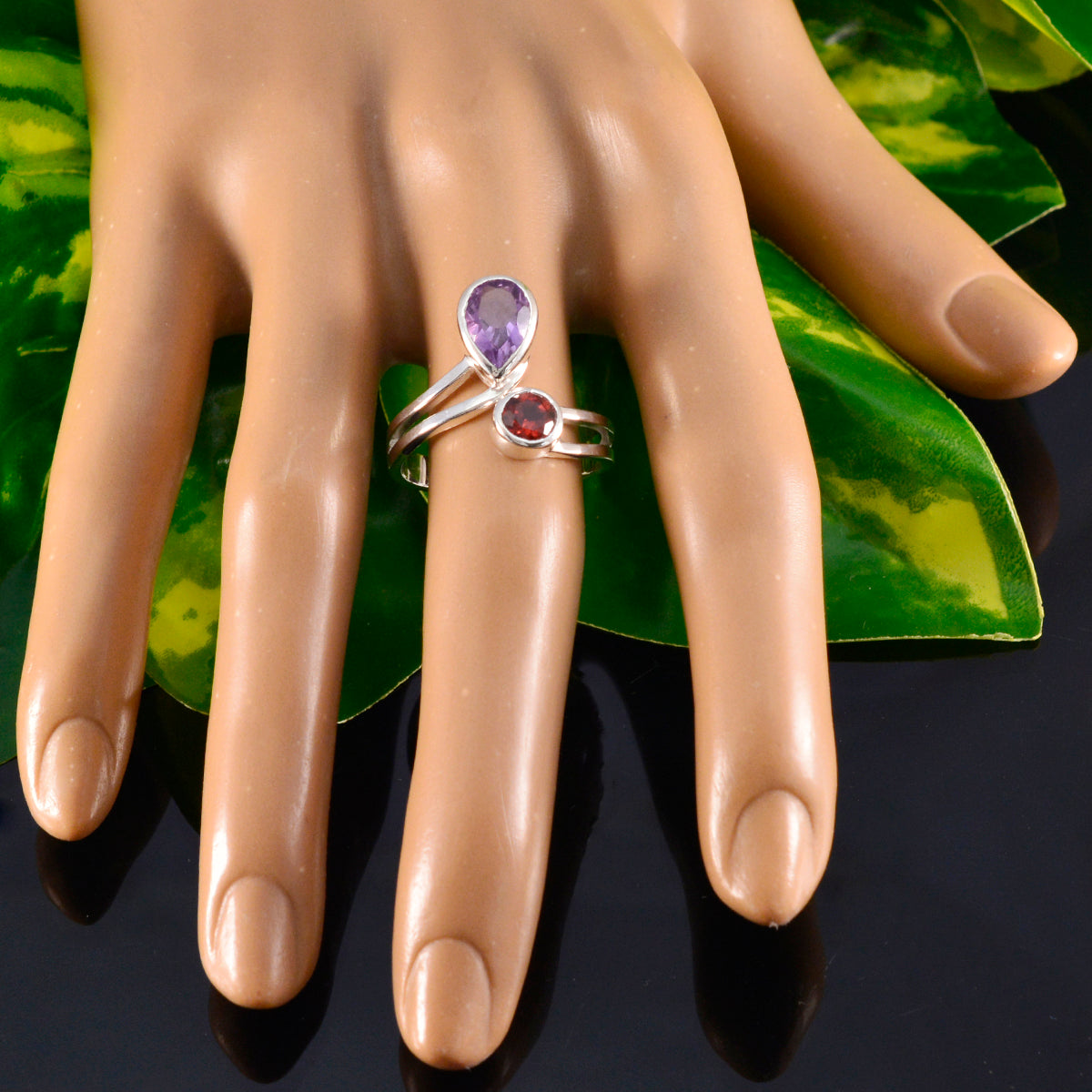 Dayana boho toi et moi ring with purple and red gemstones on a display hand against green leaves