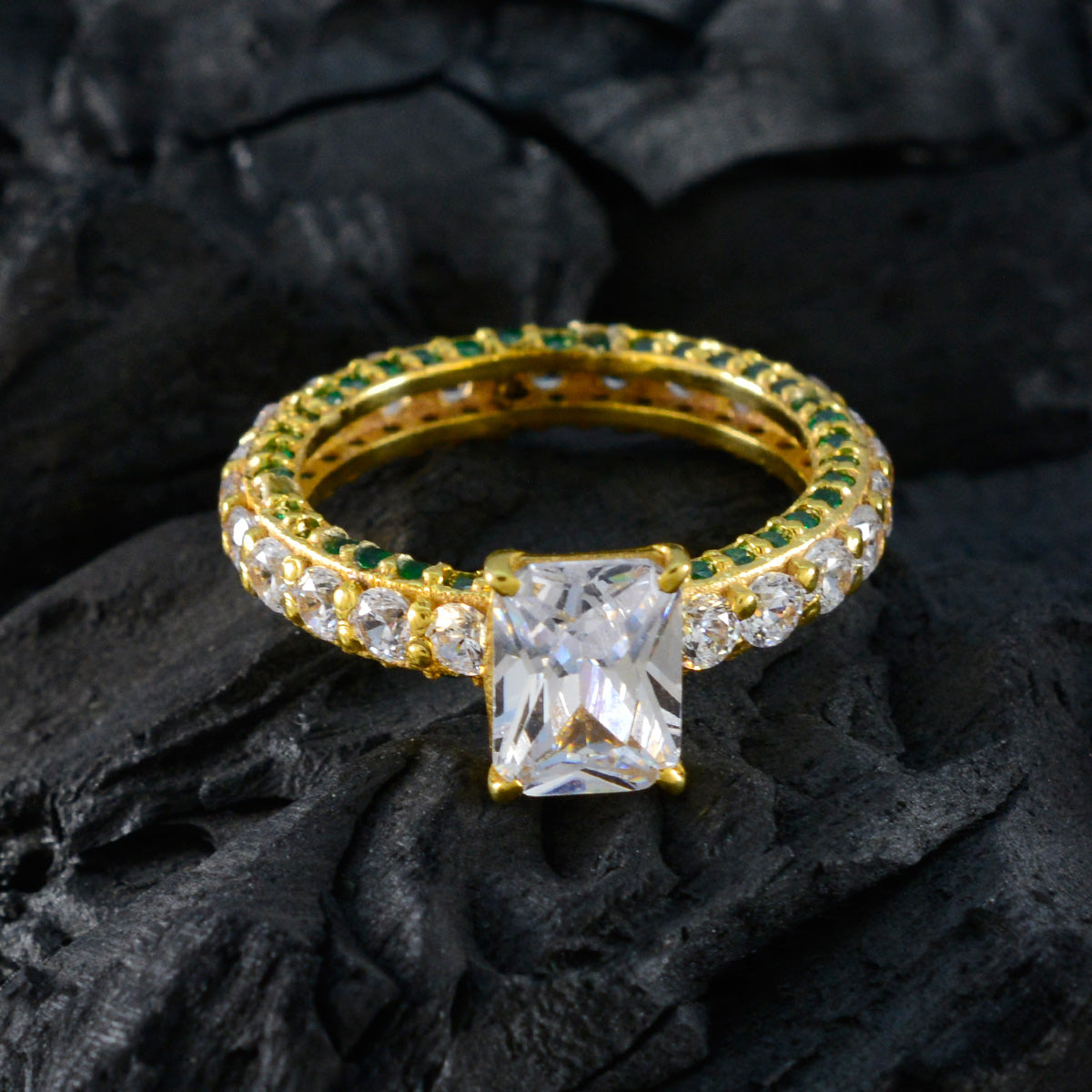 Teresa green halo engagement ring with gold band and rectangular center stone on black textured background