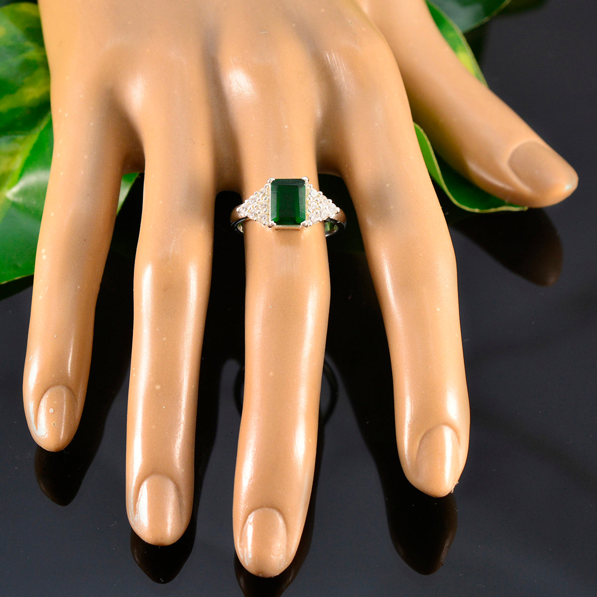 Sarah green halo ring for women with emerald cut stone and silver band displayed on mannequin hand