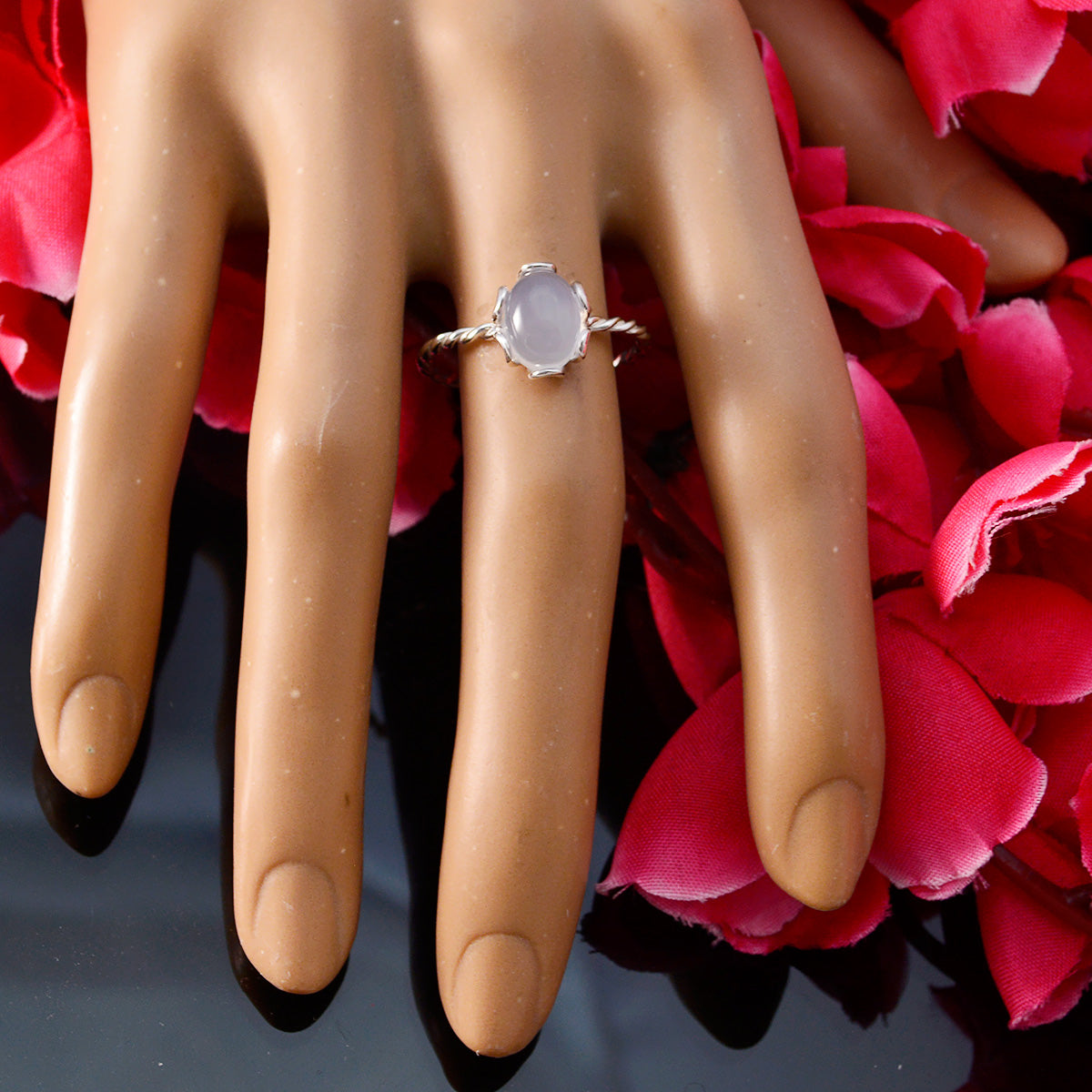 Putri aqua solitaire ring with oval aqua gemstone on a silver twisted band displayed on hand model with red petals