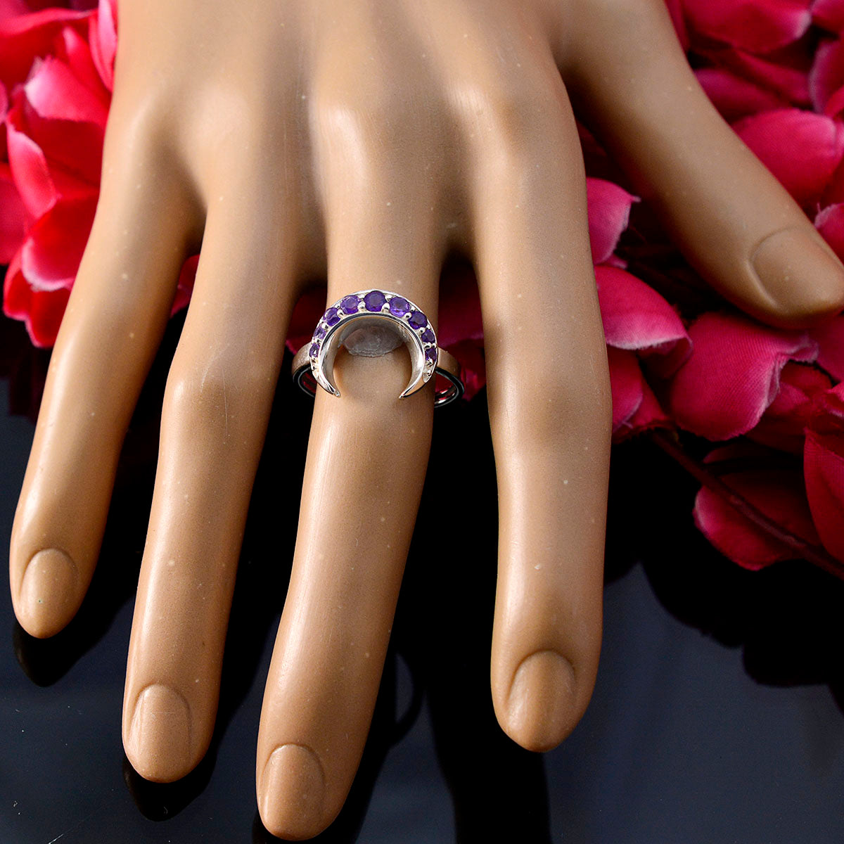 Lakshmi purple gemstone statement ring with crescent design on a display hand with pink flowers background