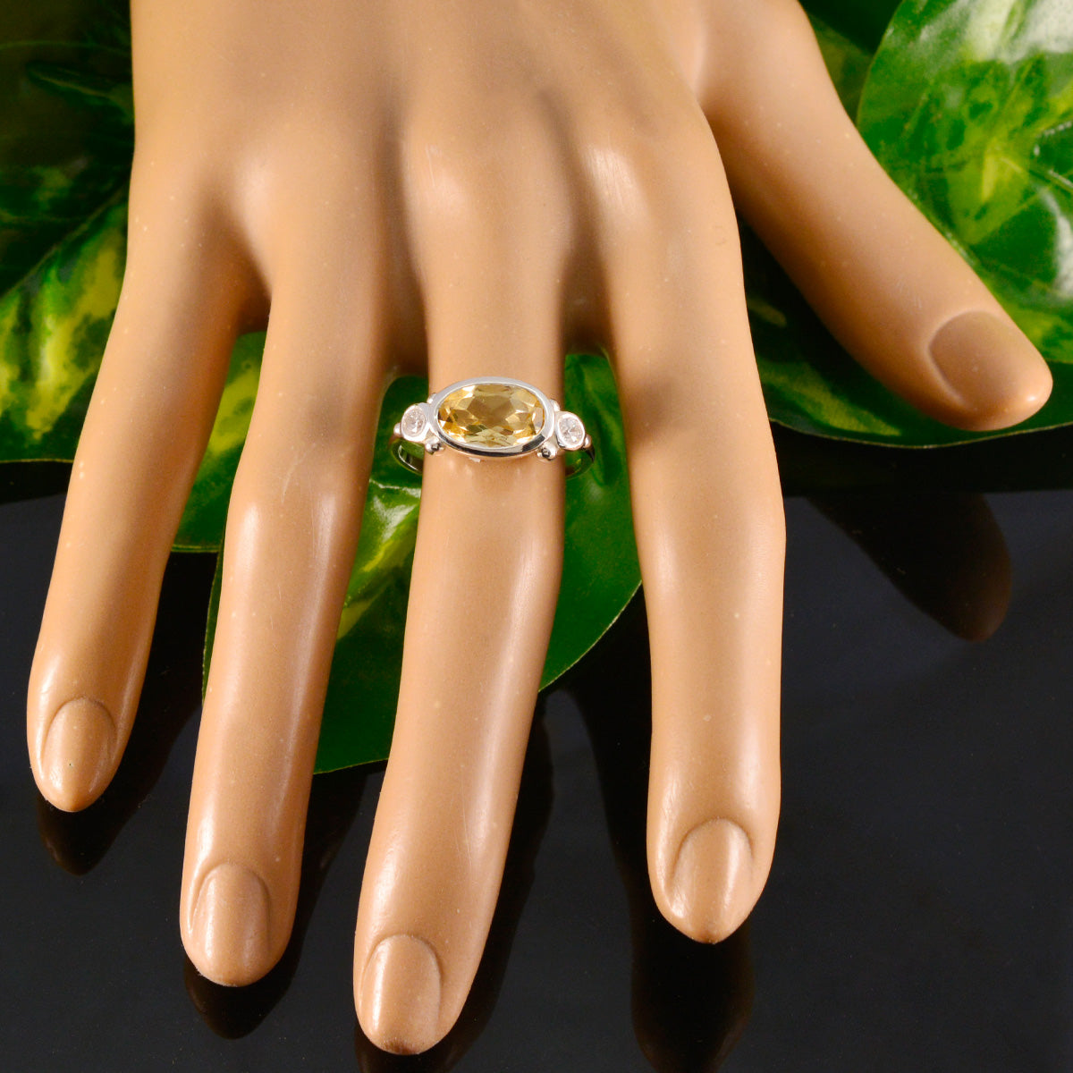 yellow gemstone trilogy ring by Hana on mannequin hand with oval center stone and two clear side stones in silver