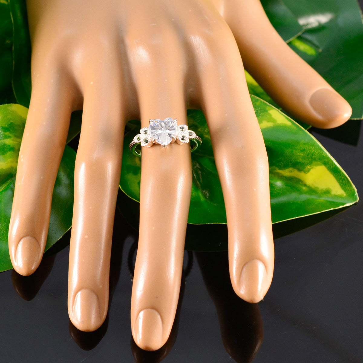 Penelope luxurious green gemstone ring on mannequin hand with floral silver band and leaf background