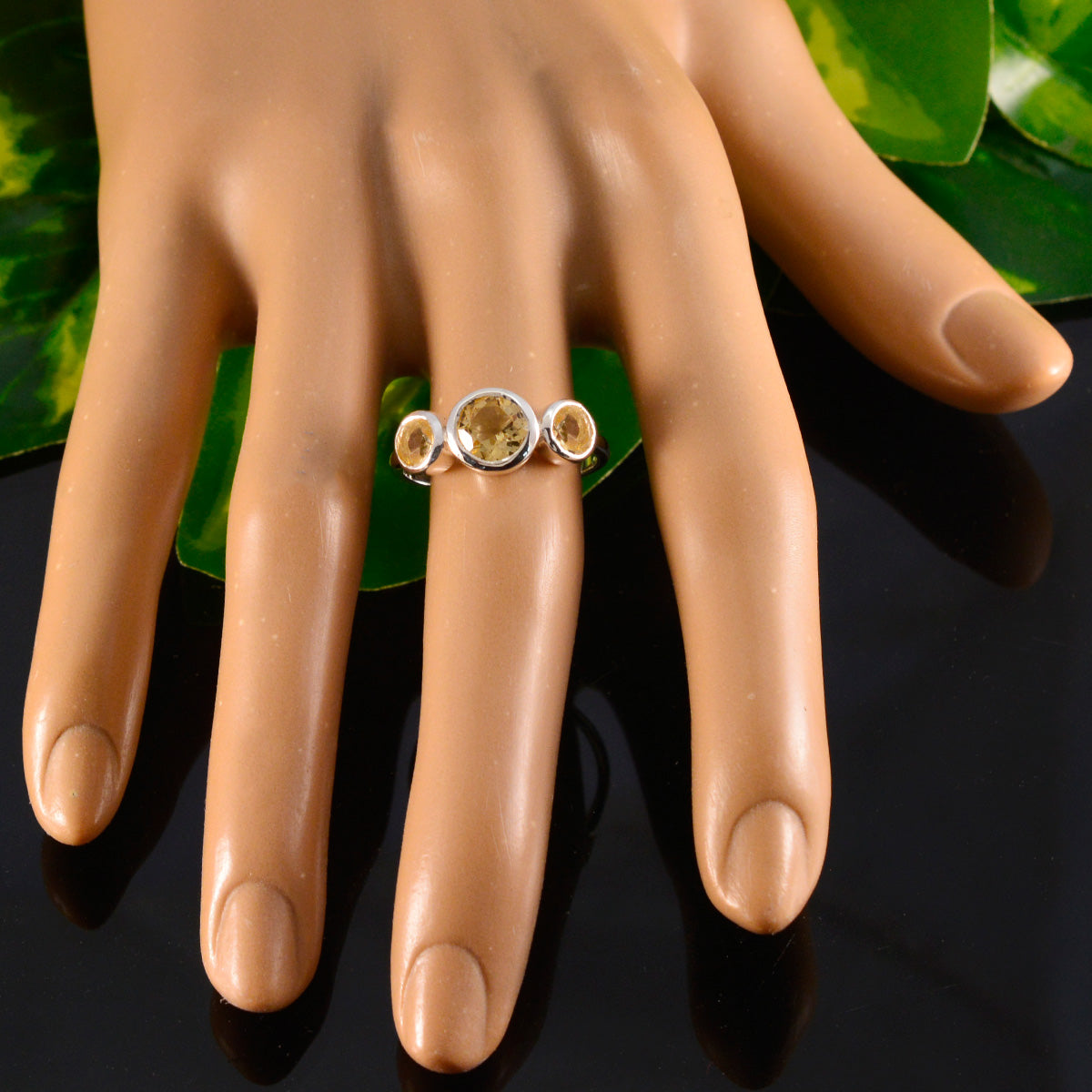 Lili modern yellow gemstone ring with three yellow stones on finger against green leaves