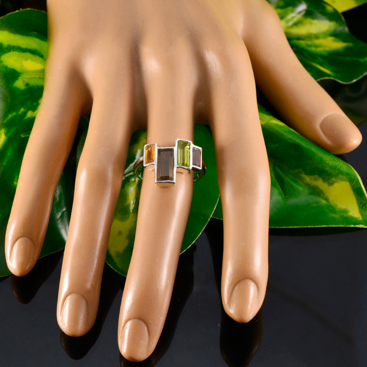 Carla multicolor cocktail ring with rectangular gemstones on a display hand with green leaves background