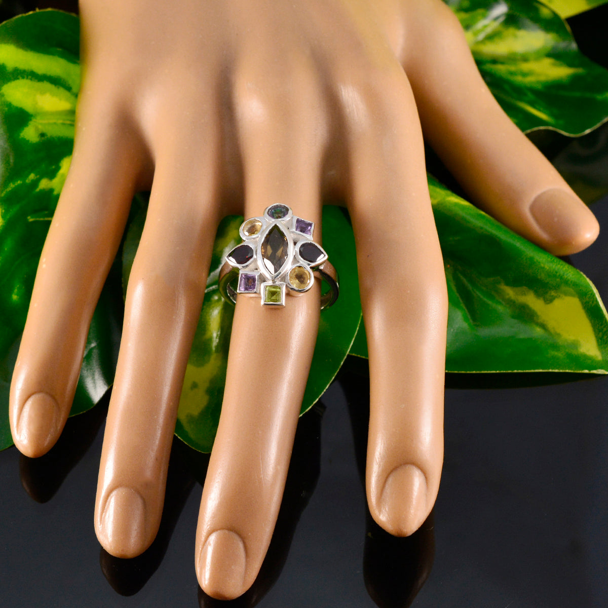 Araya multicolor navratna ring with various gemstones on a display hand over green leaves background